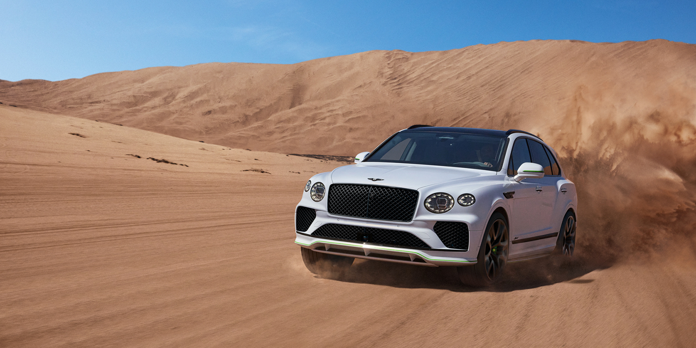 Bentley Hamburg Bentley Bentayga Speed SUV front three quarter in Snow Quarts Pearlescent by Mulliner white paint driving dynamically through the desert