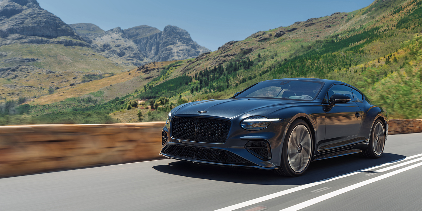 Bentley Hamburg Bentley Continental GT coupe in Thunder paint and 22" ten swept spoke wheels front 3/4 driving on mountain road