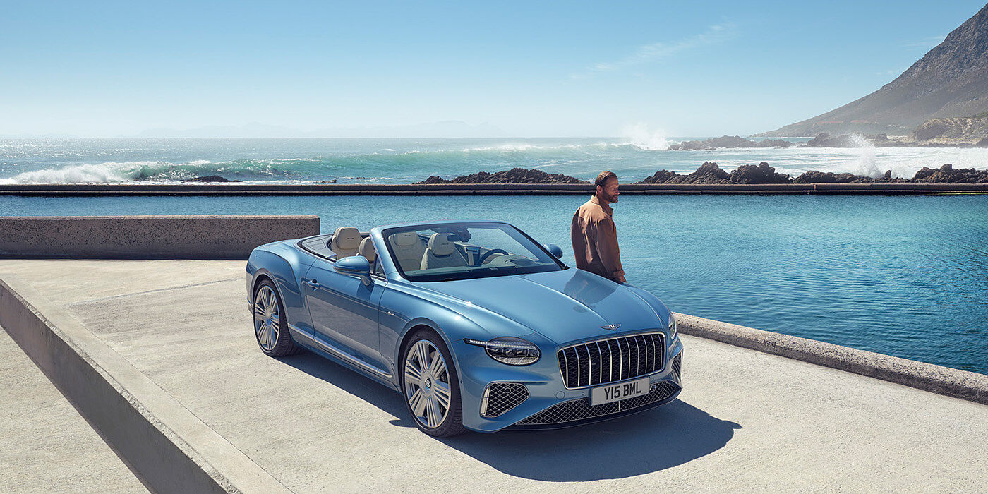 Bentley Hamburg New Bentley Continental GTC Azure convertible front view in Light Windsor blue paint with 22 inch ten spoke wheels parked by the sea in the sunshine
