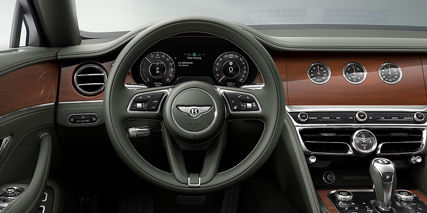Bentley Hamburg New Bentley Flying Spur sedan front cabin in Cumbrian Green hide and Crown Cut walnut veneer showing steering wheel and Rotating Display with three clocks on face