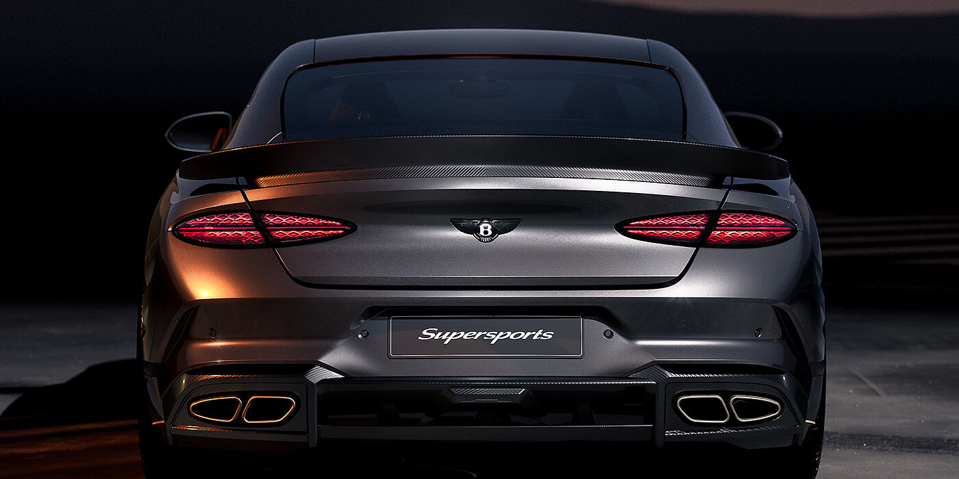Bentley Hamburg Bentley Supersports rear view with illuminated rear lamps, spoiler and black Bentley badge in Anthracite paint against a dark grey and red background