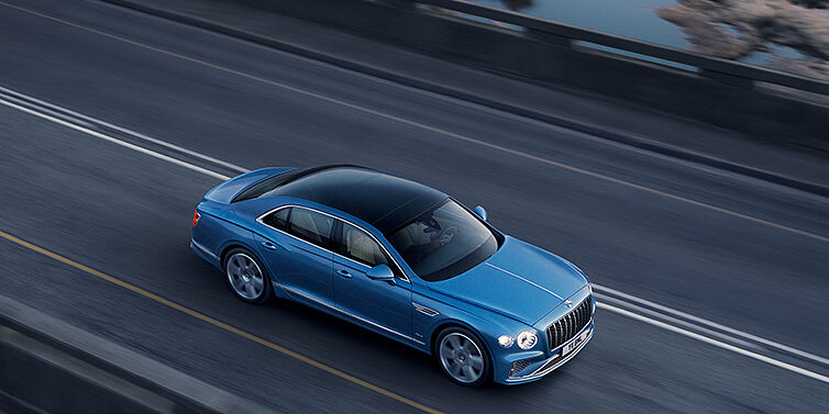 Bentley Hamburg New Bentley Flying Spur Azure sedan in Light windsor blue paint by Mulliner, with 22 inch Azure wheels seen from overhead driving dynamically on a country road