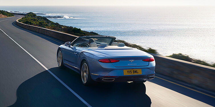 Bentley Hamburg New Bentley Continental GTC Azure convertible rear view in Light Windsor blue paint with 22 inch ten spoke wheels driving dynamically on an ocean road in the sunshine